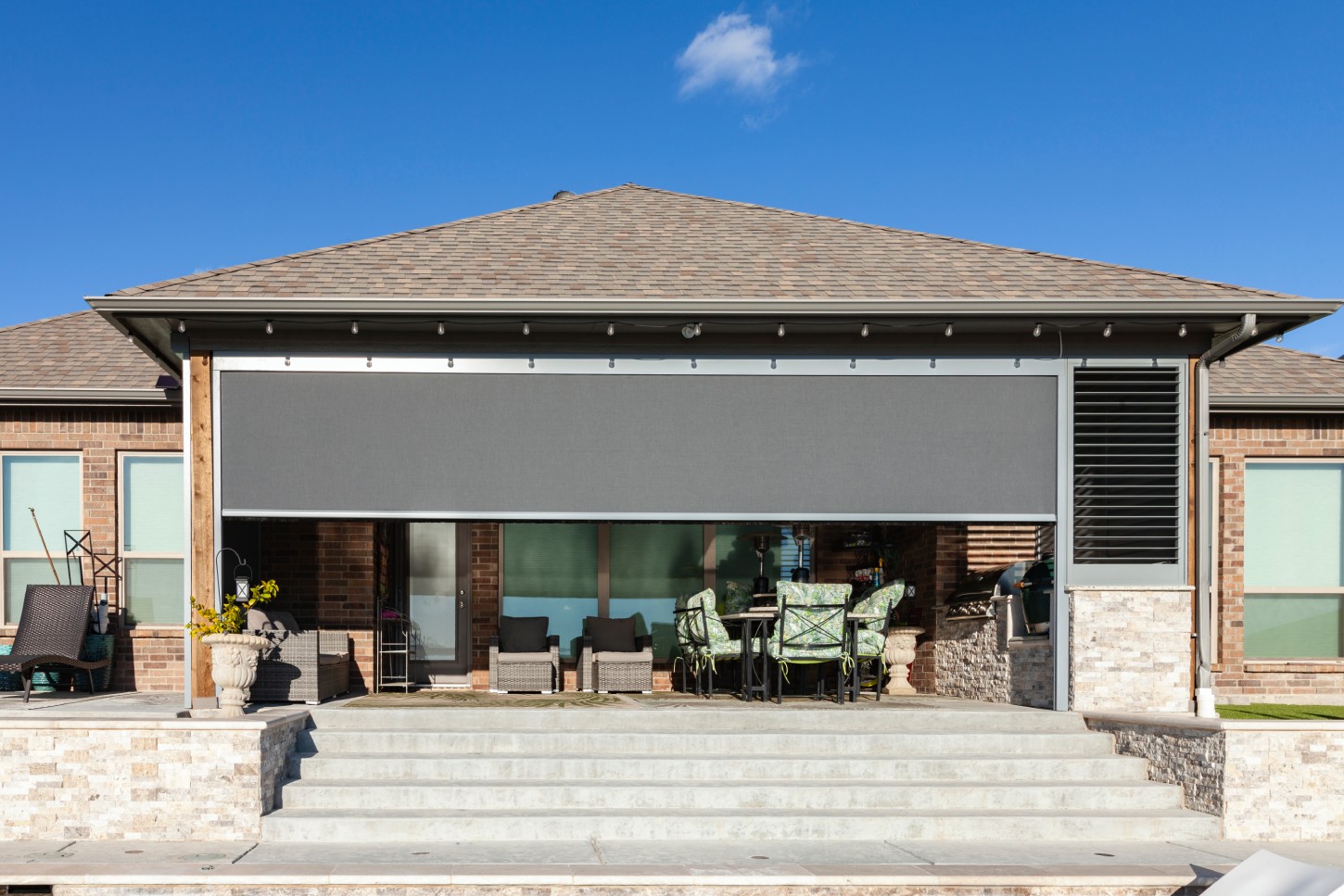 Charcoal exterior sun screen shade partially lowered on a brick home's covered patio beside a privacy screen